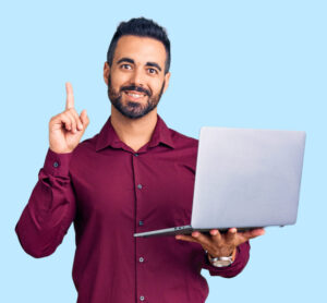 Man with dark hair and beard points to the sky while holding his laptop. He seems to have had a moment of realisation. Image taken from Adobe Stock.