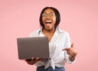Woman looks extreamly happy as she points to her laptop. Image taken from Adobe Stock